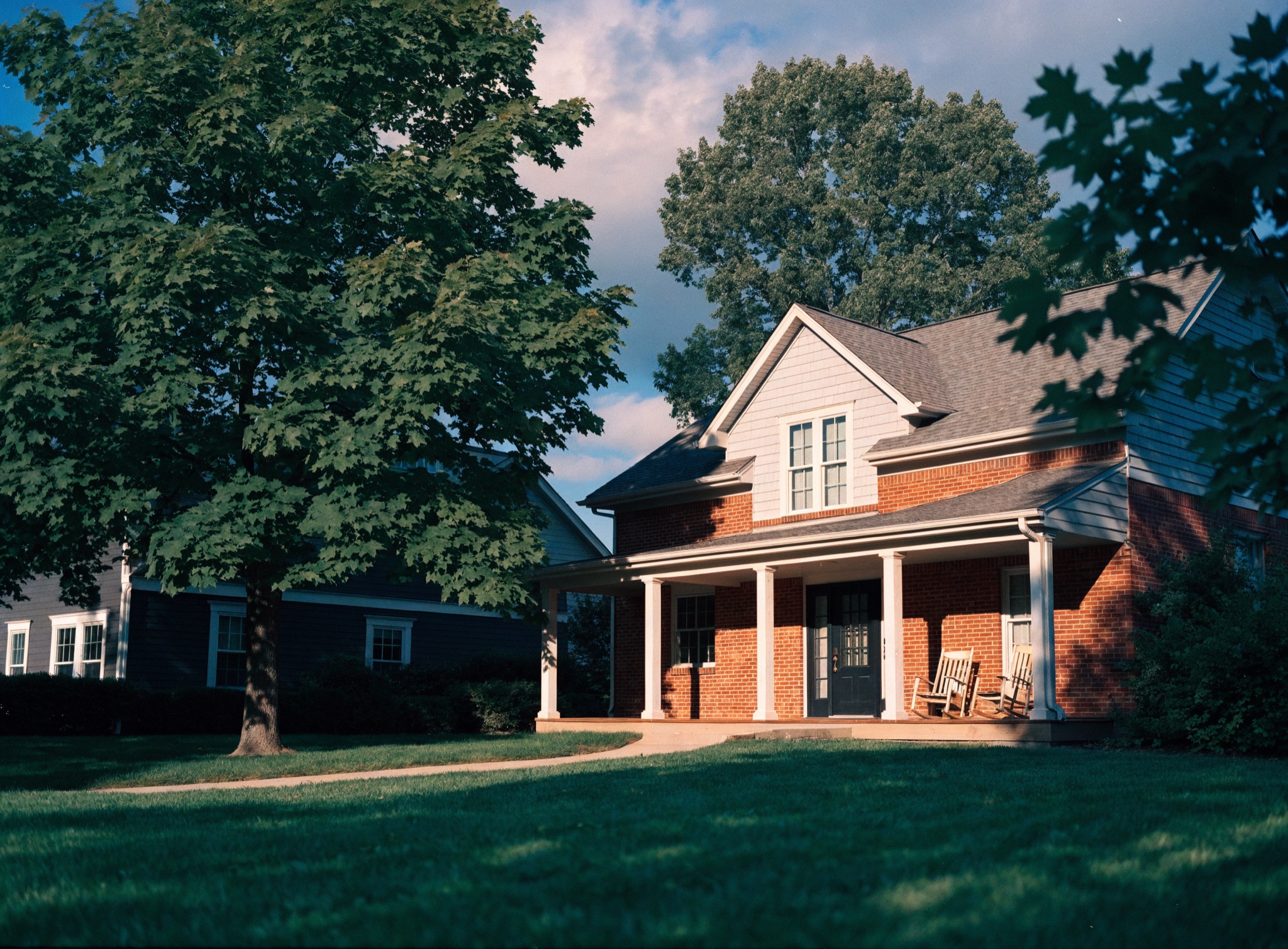 An established red-brick family home with a covered porch under a mature maple in late-morning sun